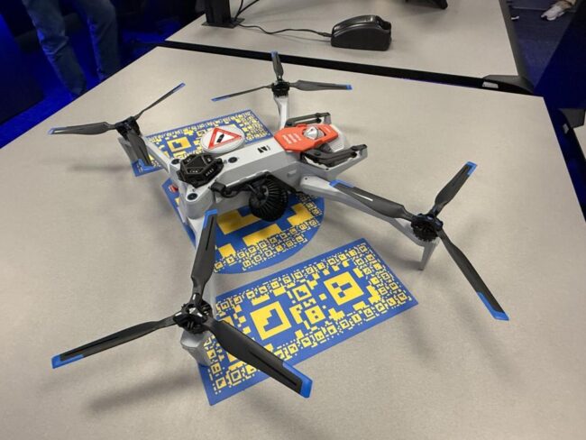 Drone Quadcopter drone with four rotors on a table, with blue-and-yellow QR code cards underneath it.